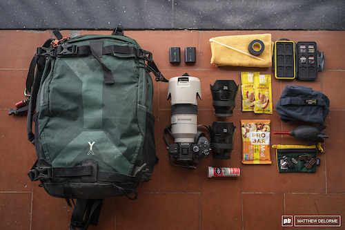 Matthew DeLorme's set up for a typical day of shooting EWS. NYA EVO Fjord 36 camera bag. NYA EVO is a relatively new bag company. Their philosophy is to make a rugged bag with as little environmental impact. The pack rides well and doesn't push up on the back of the helmet when the going gets steep. 

Inside: Sony A7III,  Sony 70-200 2.8 G Master, Zeiss Batis 18 2.8, Zeiss Batis 25 2, Rocket Air ProBar Meal Bar, ProBar Siracha Peanut Butter, electrolyte tabs, electrical tape, quick link, brake pads, batteries, Co2 head, zip tie, tape, towel, lens coat rain cover. If the weather looks iffy, I'll bring rain gear as well.