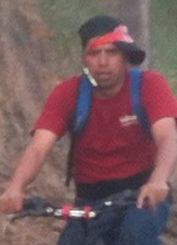 Zoomed in to see man riding bike while talking on the phone. It looks like the phone is taped to his head with what looks like electrical tape?