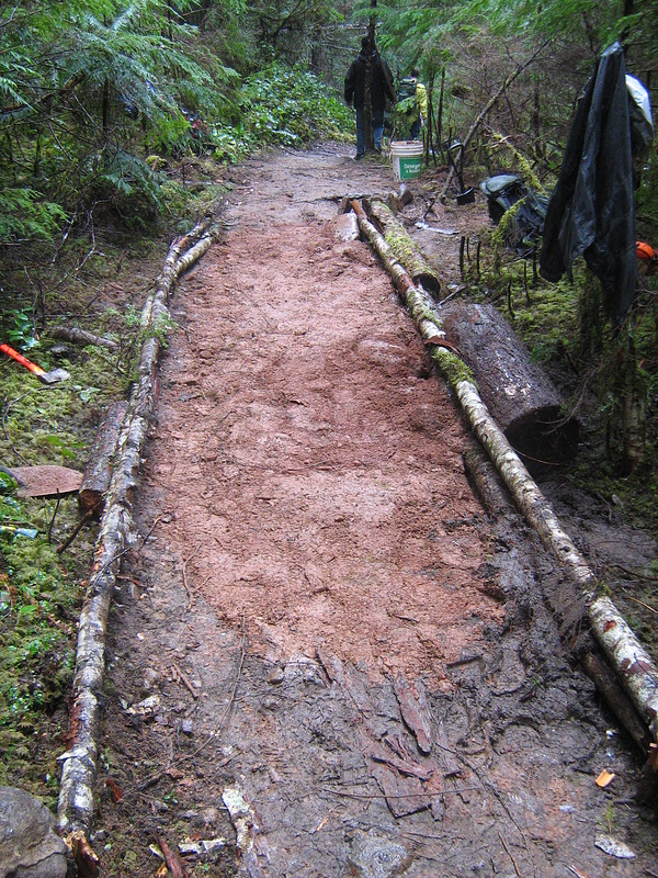 "After" pic with an armoured section with drainage to the right hidden under the trees draining off to a trench cut through sandstone by the bucket.
