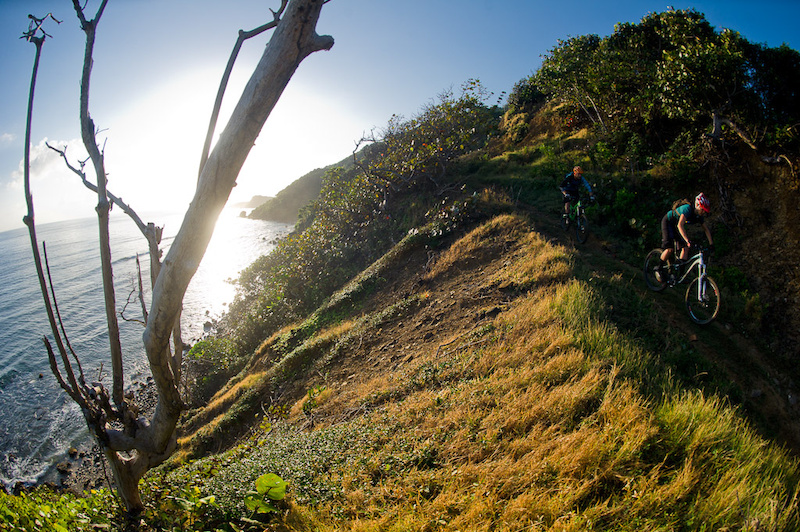Seb Kemp and Katie Holden ride their bikes on a trail above the ocean near Robin's Bay in Jamaica at sunrise.