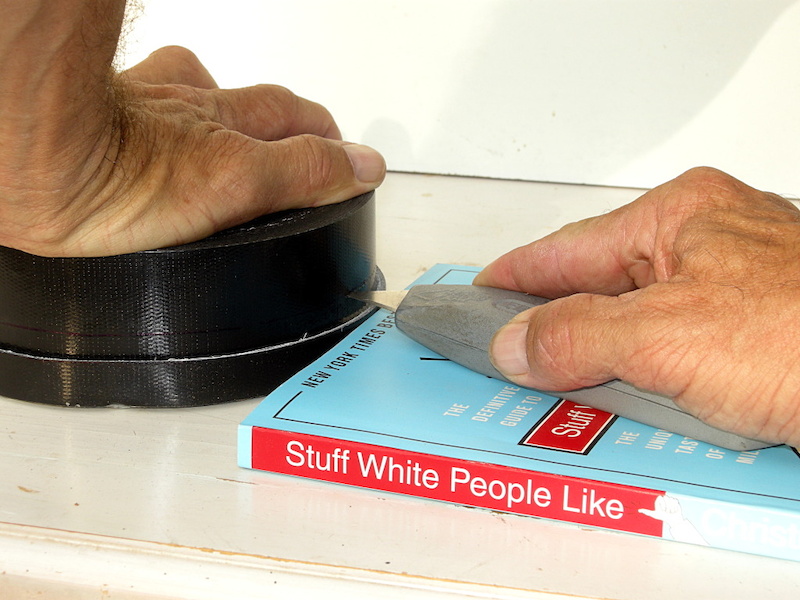 Find a New York Times Best Seller or piece of wood that will space the box knife blade to the line on the tape. Hold the knife securely and slide it across the book about an inch at a time to slice the tape to the proper width. Go around two or three times to ensure that you ll have enough length to get around the rim.