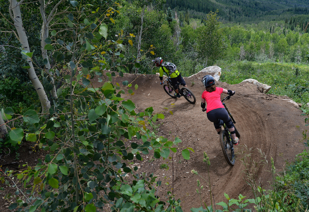 Steamboat Bike Park instructor Tim Price leads Nicole Miller through a banked turn on Rustler Ridge, a blue downhill trail in the Steamboat Bike Park.