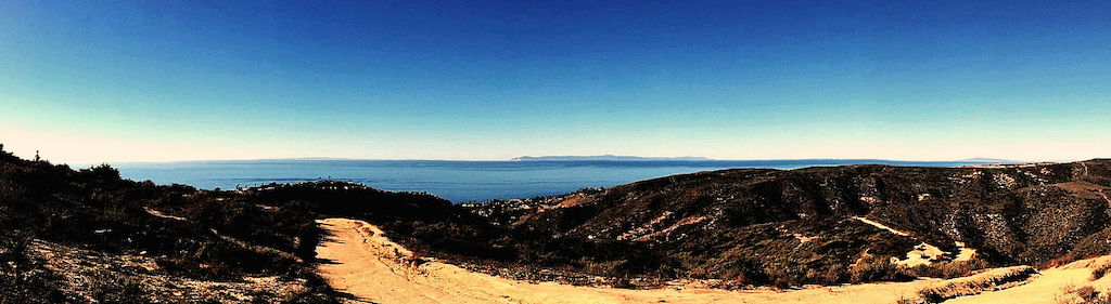 A very clear day at Top of the World in Laguna Beach. On the horizon in the center is Catalina Island, to its left is San Clemente Island, and to the right in the distance is Signal Hill in Long Beach. On the far left you can see the silhouette of a pregnant woman who hiked down the trail to admire the view.