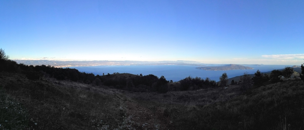 A panoramic view of a blue sea and distant islands from a hillside at sunset.