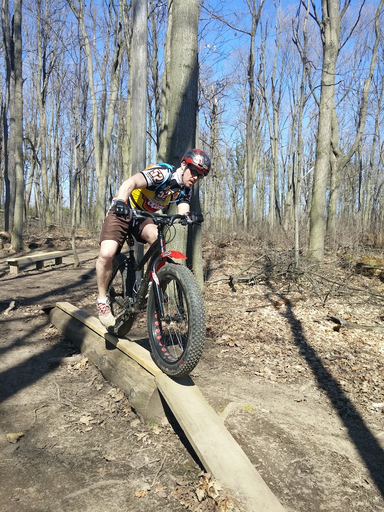 A mountain biker riding across a wooden skinny feature in a bare deciduous forest.