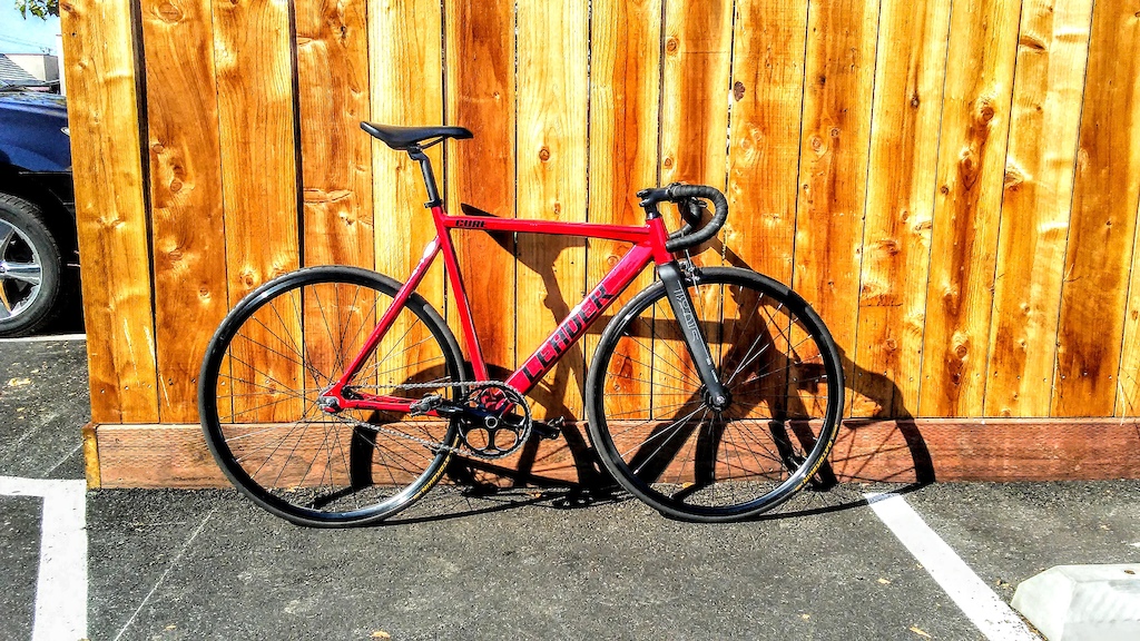 New red bicycle with colored flake, race-prepared and race-ready. Gatorskin tire set 23mm. Flip-Flop rear hub. Freewheel: 17 tooth. Fixed: 16 tooth. 48 tooth crankset. Carbon fiber front forks. 26" wheels, 31" ground to top frame