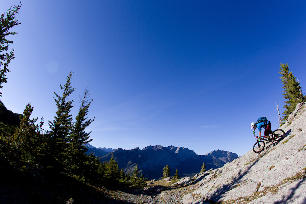 A male mountain biker rides a rock slab on a cross country trail on a sunny day.