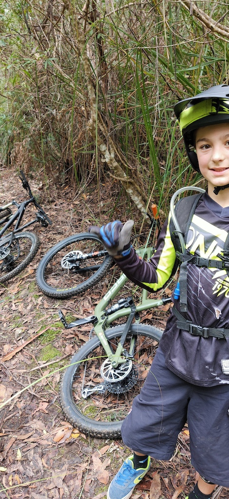 A young mountain biker poses with their bike in dense forest vegetation.
