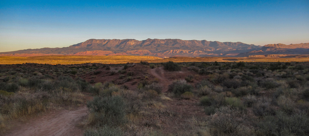 Wide desert valley view with mountains lit by morning sun on horizon.