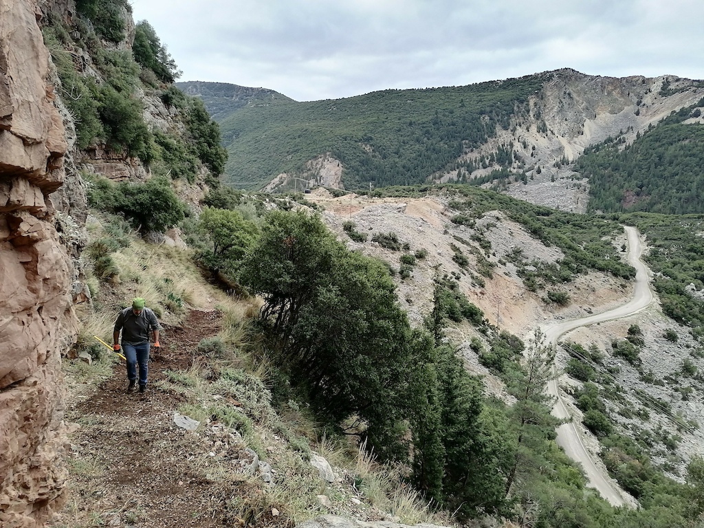 A hiker walking along a narrow path high above a winding river valley in a canyon.