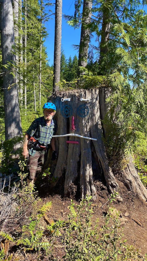 One of Cumberland's iconic trial builders, Al Munday, of the local legendary River Rats trail building crew standing next to a bike art portrait meant to resemble Al, located on Thirsty Beaver, one of many signature River Rats trails.