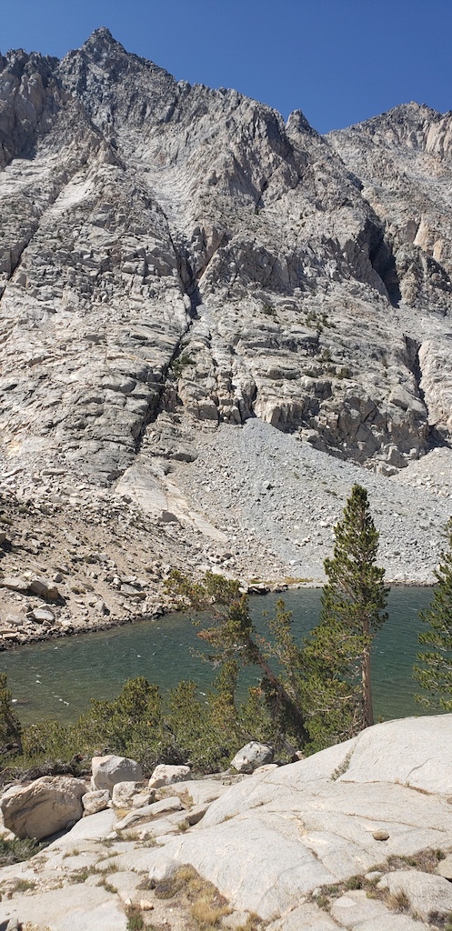 Alpine rocky terrain with a mountain lake surrounded by granite peaks under blue sky.