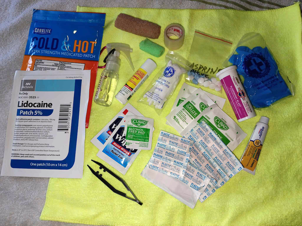 Here is my basic First Aid kit that I carry with me, while Mnt. Biking. I pack these items in my Hydration Pack:
* Hand sanitizer, and/or rubbing alcohol, as well as 3-6 pieces of Alcohol pads
* Topical anesthetic ointment
*Bandaids (various sizes, and shapes). 
* Sterile or clean gloves (latex or non-latex is your preference)
* Gauze and/or sterile cotton balls, & Q-tips
* Tweezers
* A few of each - Ibuprofen, Aleve, & Aspirin
* A few strips of stretchy wrap, and/or Elastic bandage, 1 roll each of small & medium sizes
* Glucose Tablets, It’s good to have some emergency” - “Carbs/Sugar” in case you get hypoglycemia ("BONK").
* Meanthal Topical rub to alleviate sore muscles
* Icy/Hot patches
*Lidocaine patch, a topical pain relief patch.