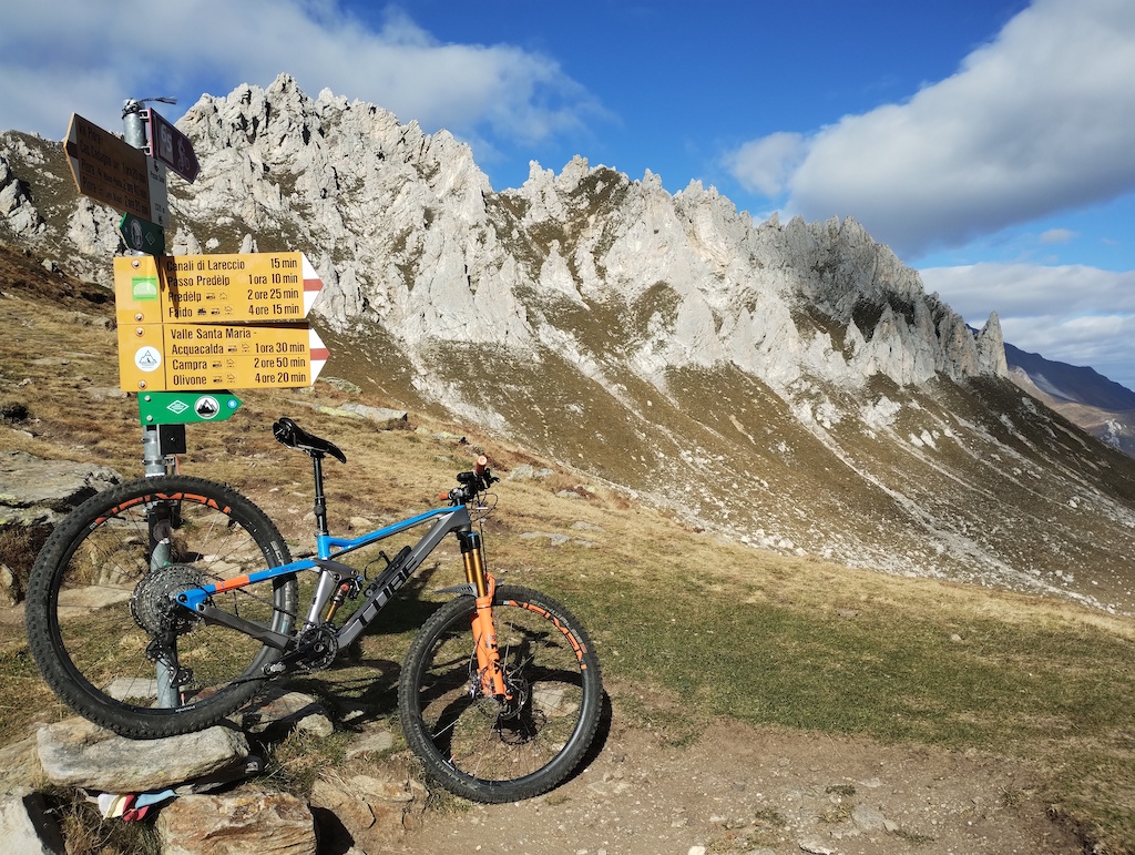 Mountain bike at trail sign near white rock cliffs and alpine meadow.