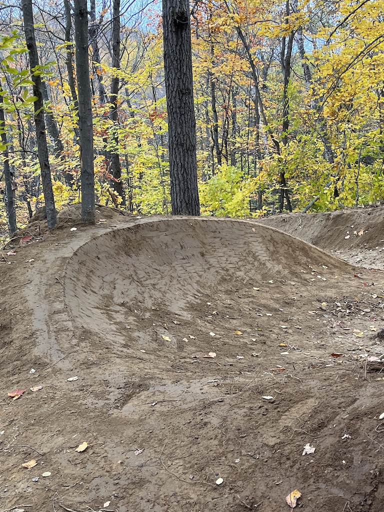 A large bermed turn through a forest with fall foliage in the background.