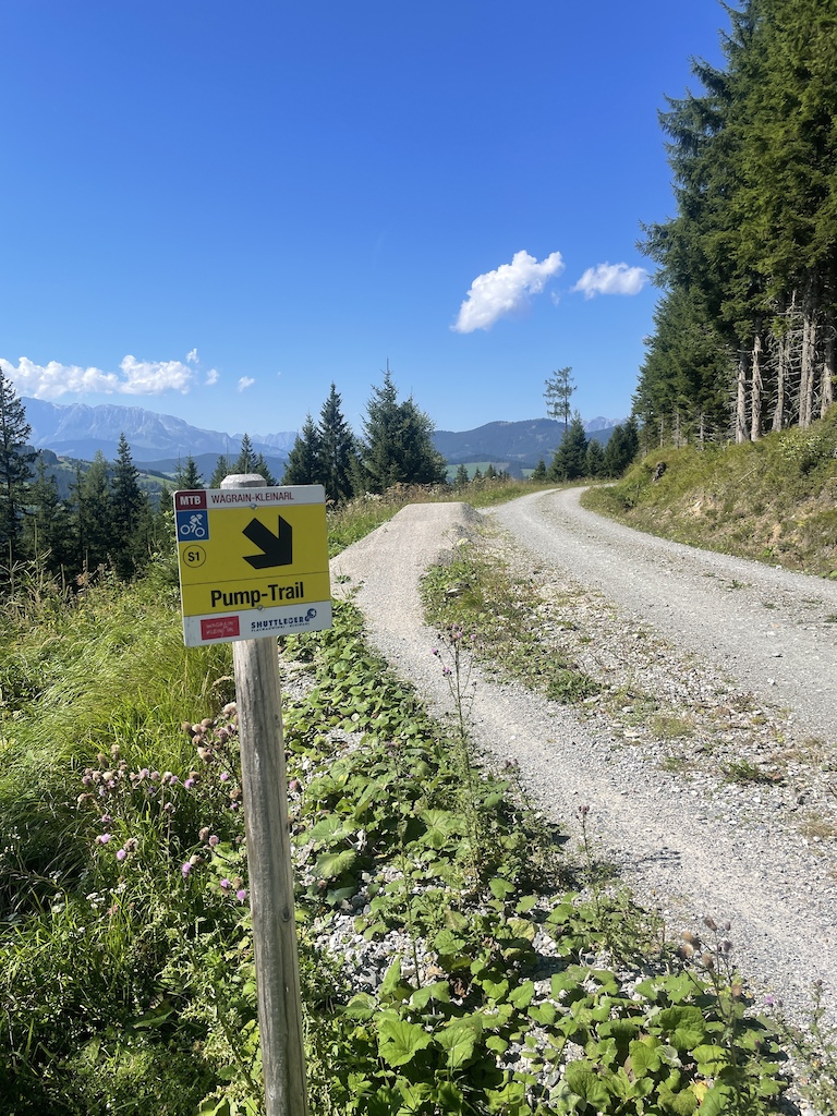 A gravel trail with a yellow Pump-Trail sign showing downward arrow direction.