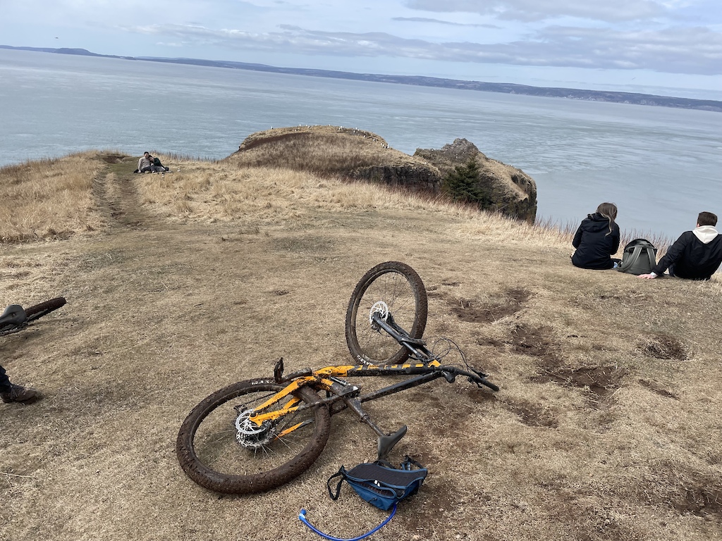 A mountain bike and people resting on a grassy overlook above a bay.