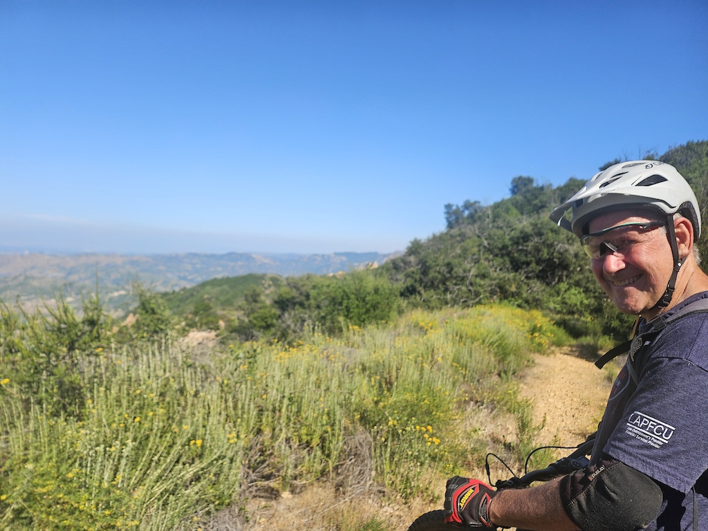 A cyclist posing on a gravel trail overlooking hillside valleys.