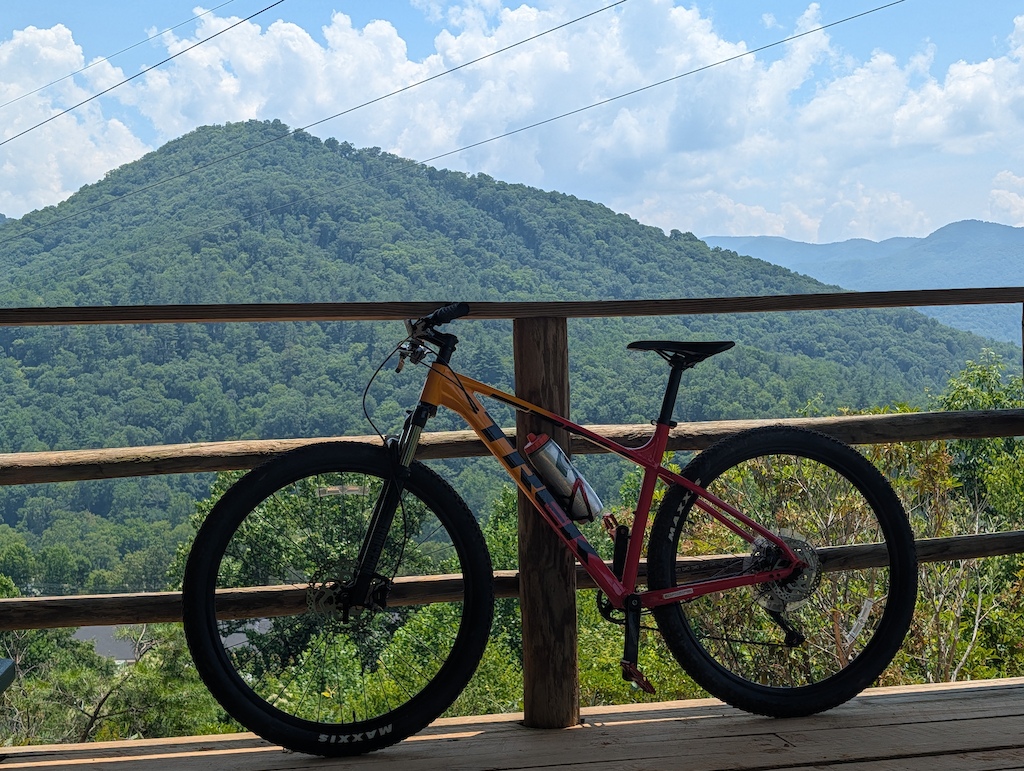 A mountain bike rests against a wooden railing on a scenic overlook.