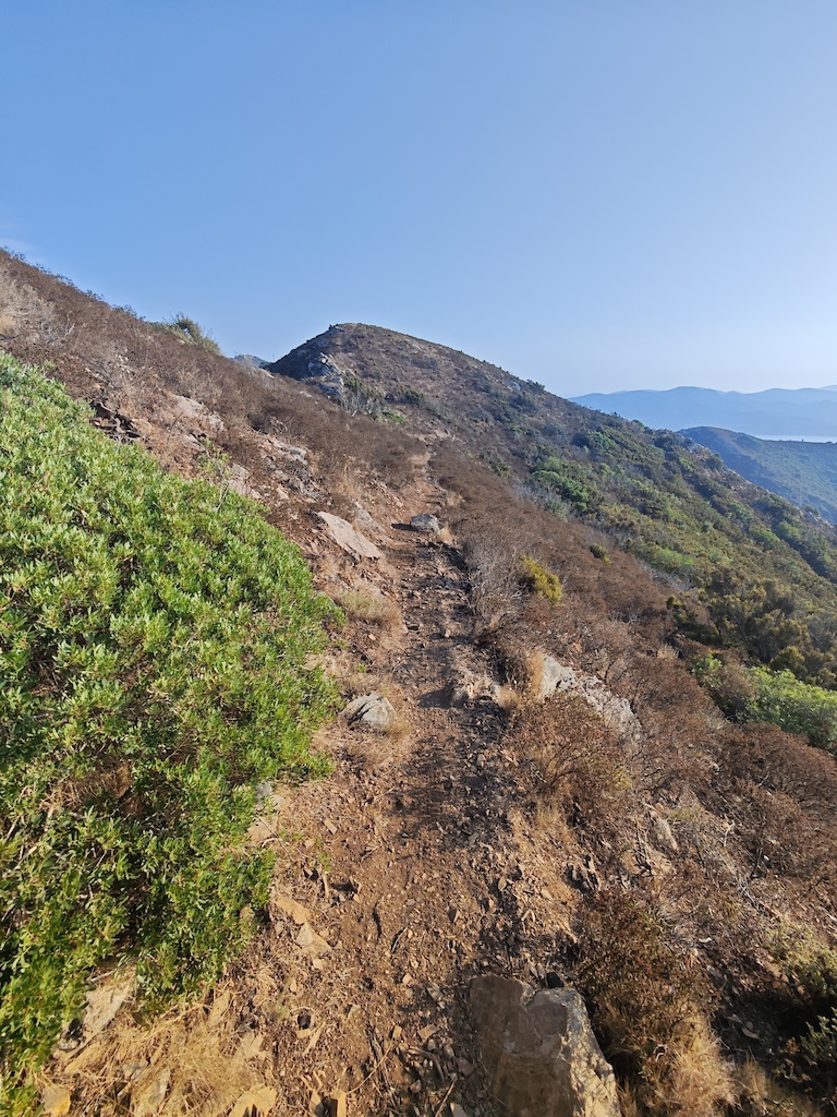 A hiker on a rocky ridge with mountains and valleys visible in the distance.