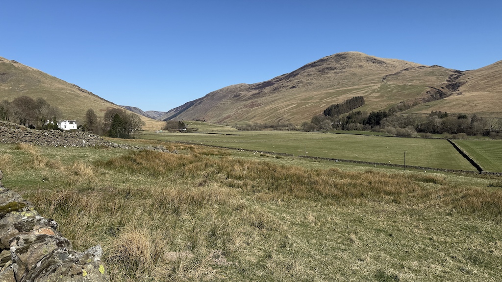Open valley with green fields, distant hills and scattered trees along the horizon.