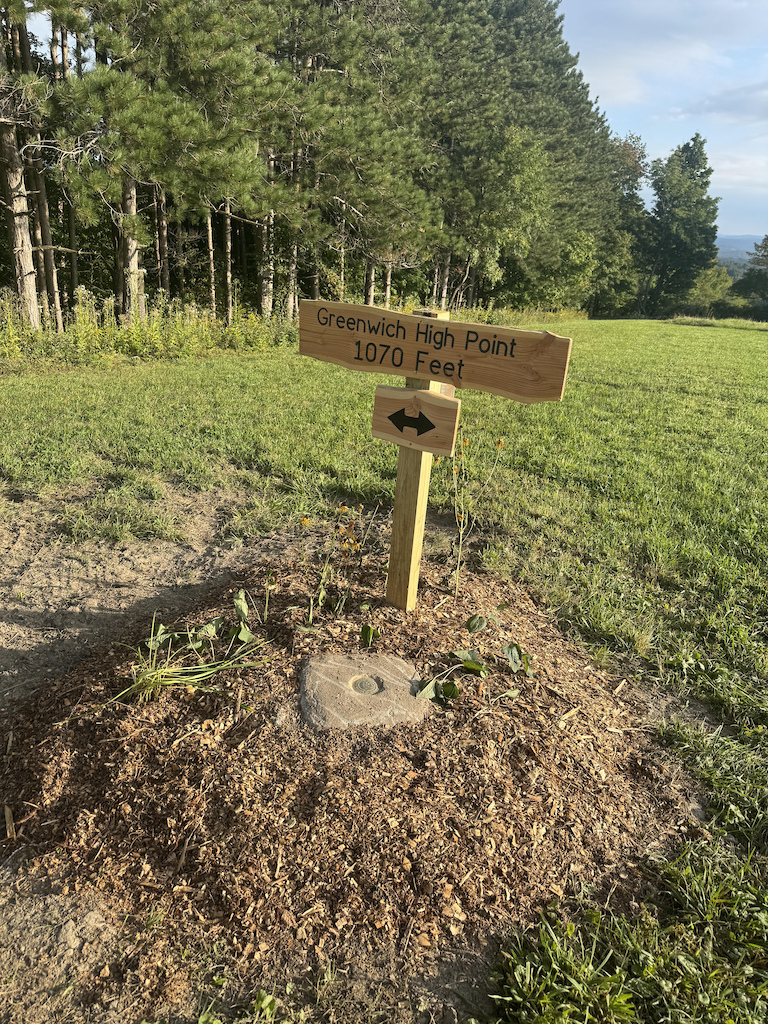 A wooden sign at Greenwich High Point reading 1070 Feet with an arrow, in an open meadow.
