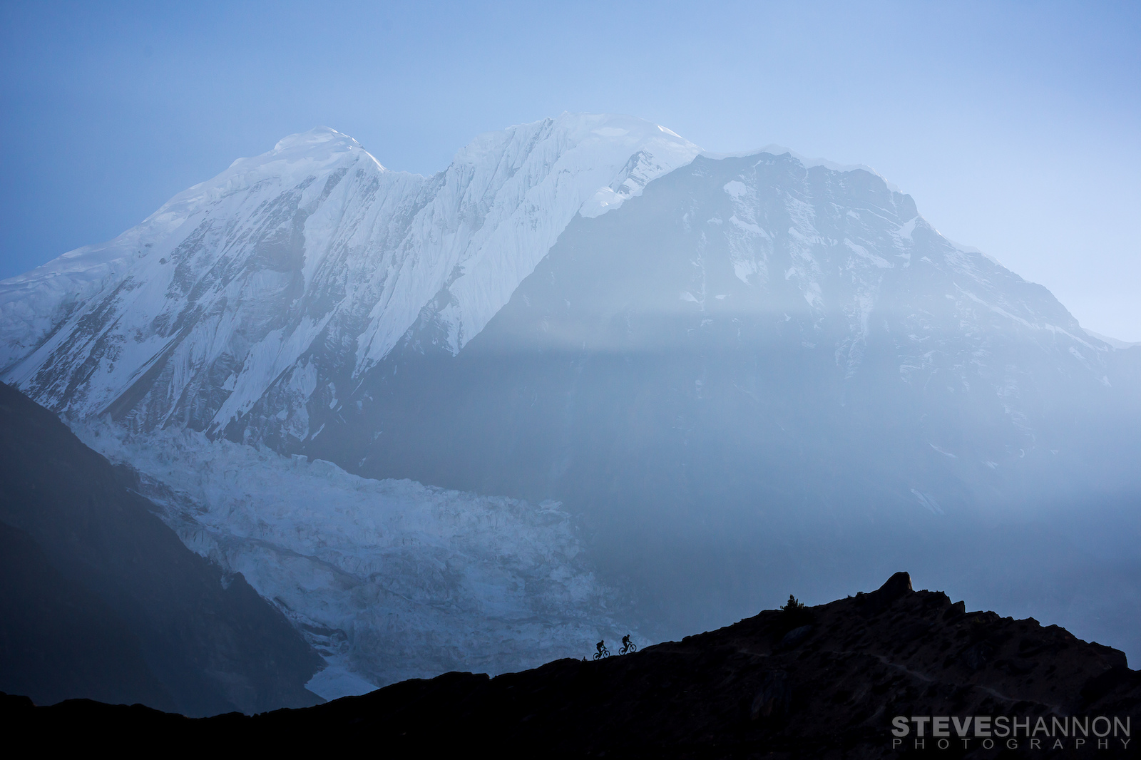 Mountain bikers silhouetted against the massive Himalayan peak, Gangapurna (7455m).