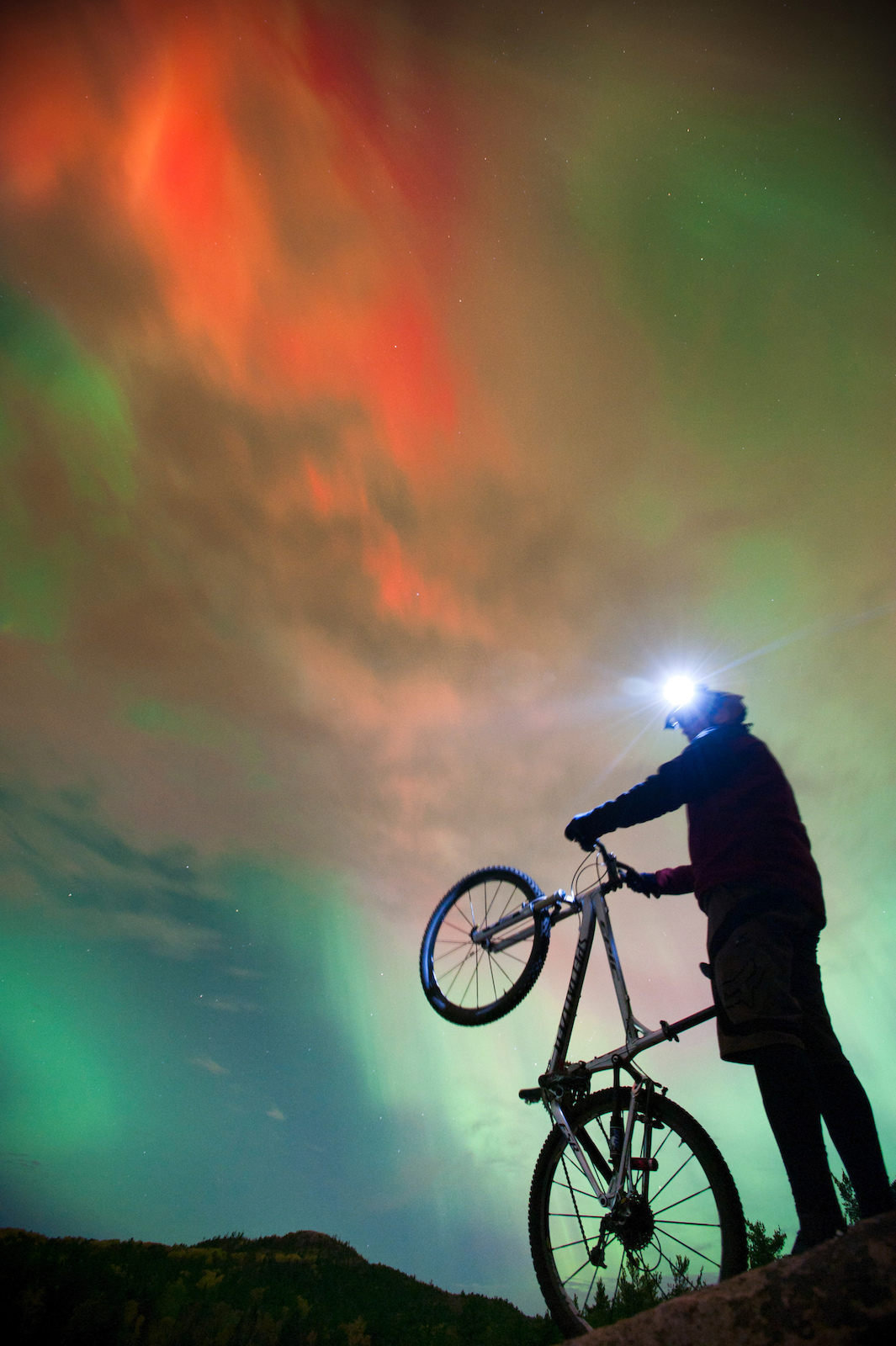 Night mountain bike riding with aurora borealis northern lights near Marquette Michigan.