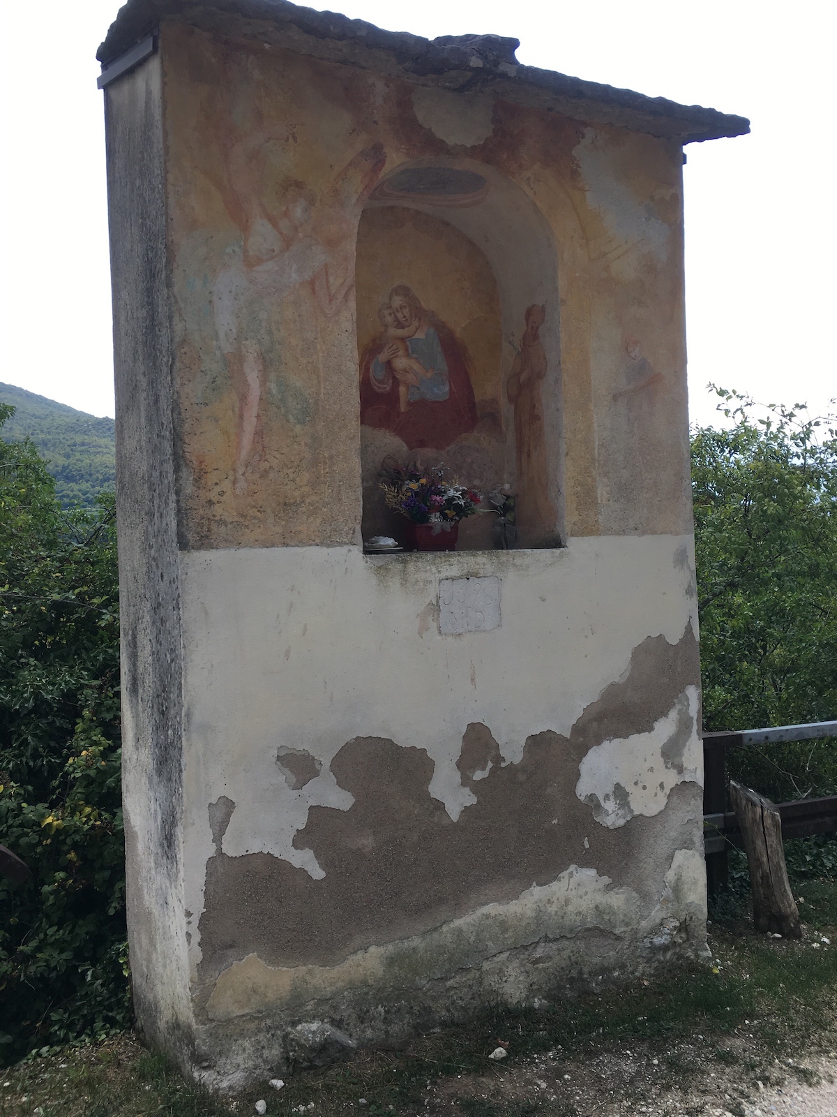 A weathered stone chapel or shrine with religious artwork on a hillside.