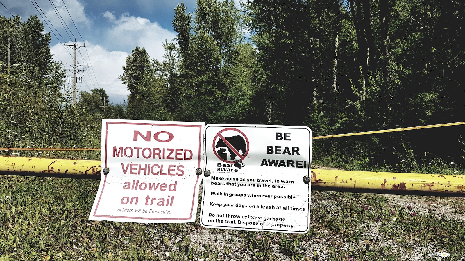 Trail signs reading "No Motorized Vehicles" and "Be Bear Aware" posted on a yellow pipe.