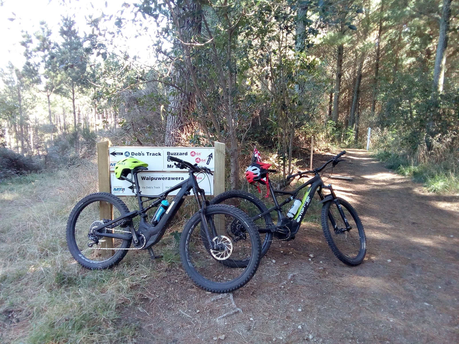 Two electric mountain bikes leaning against a trail sign in a forest.