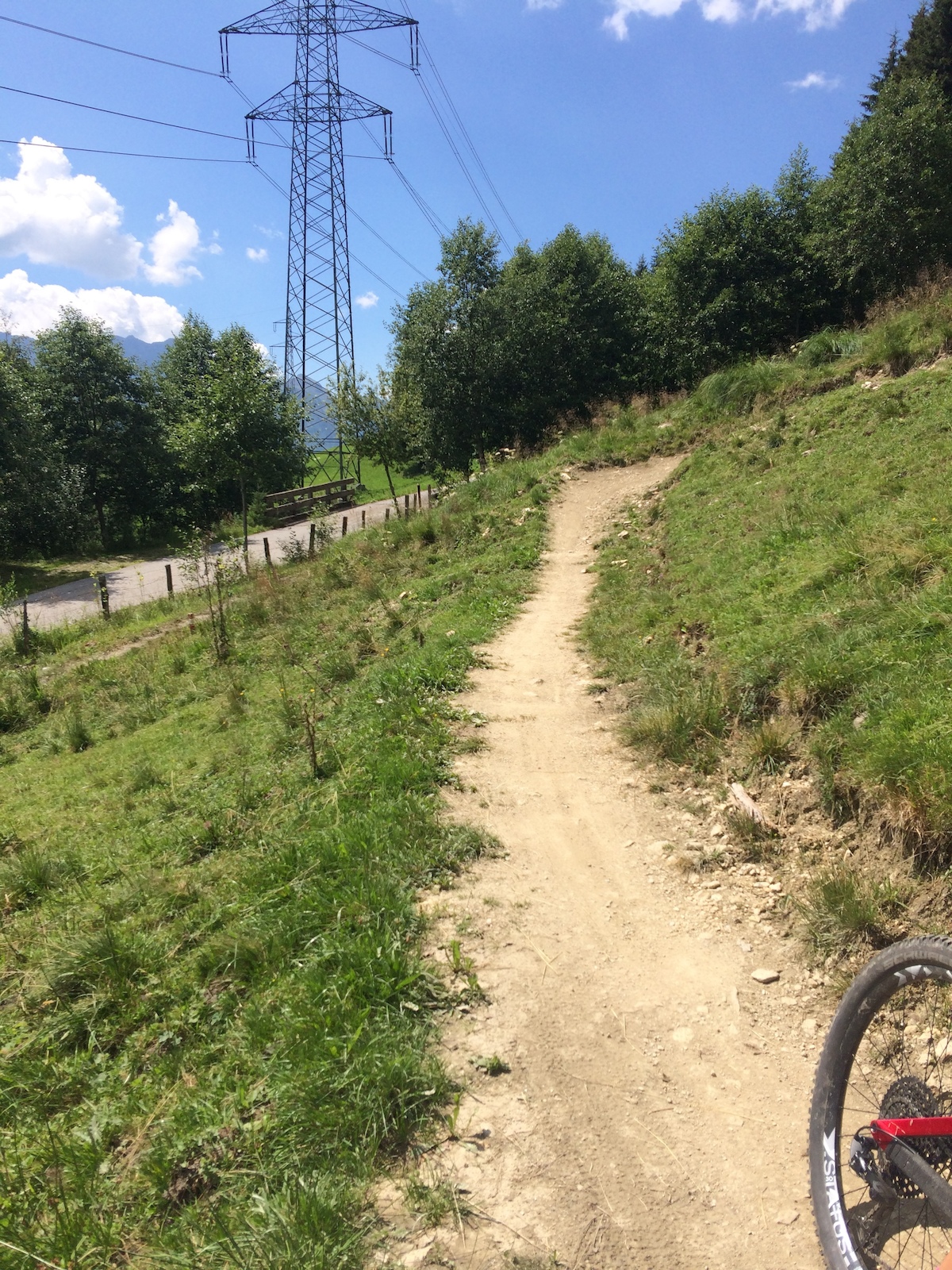Partial view of a bike wheel on a gravel trail below a power transmission tower.