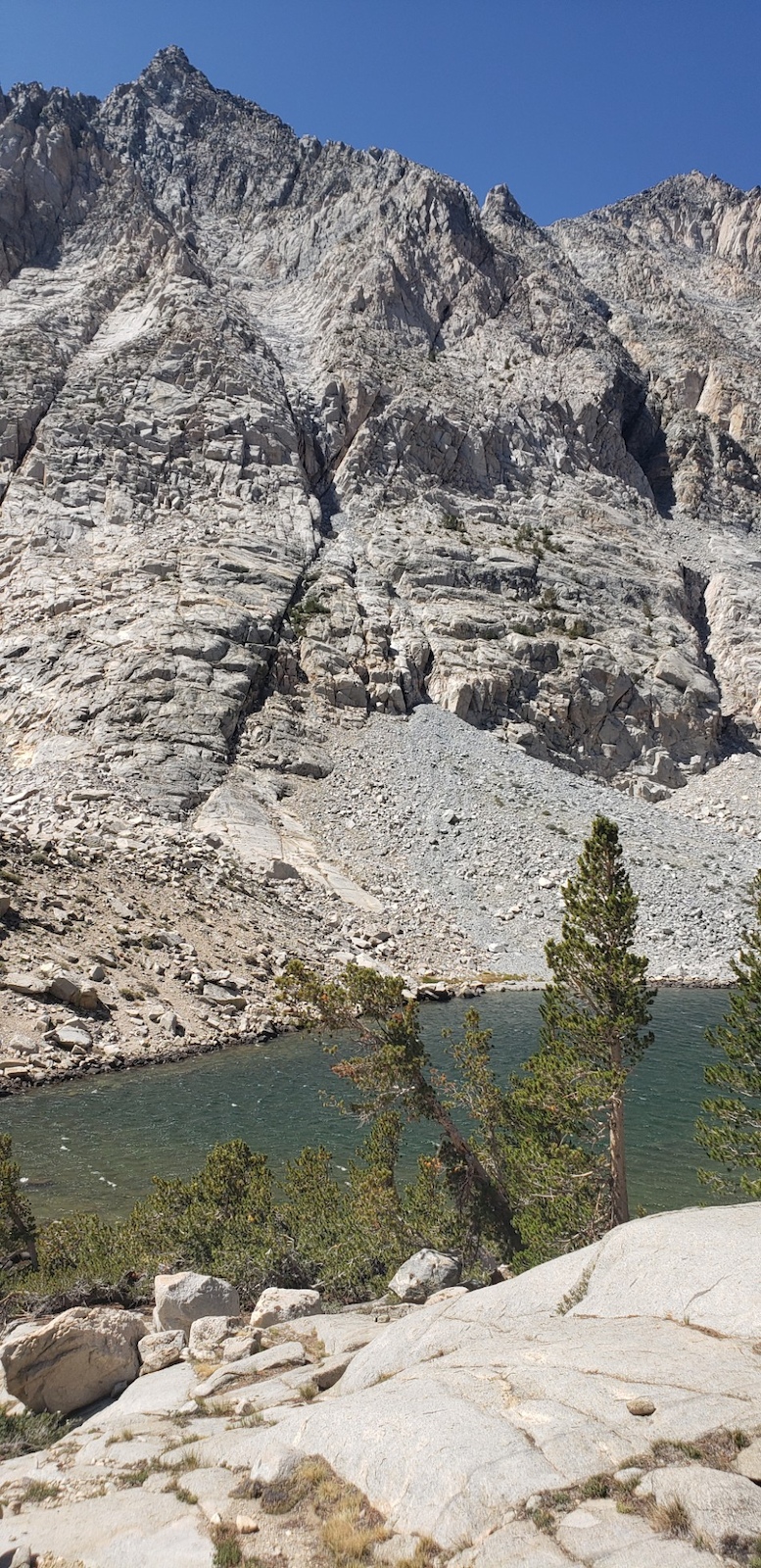 Alpine rocky terrain with a mountain lake surrounded by granite peaks under blue sky.