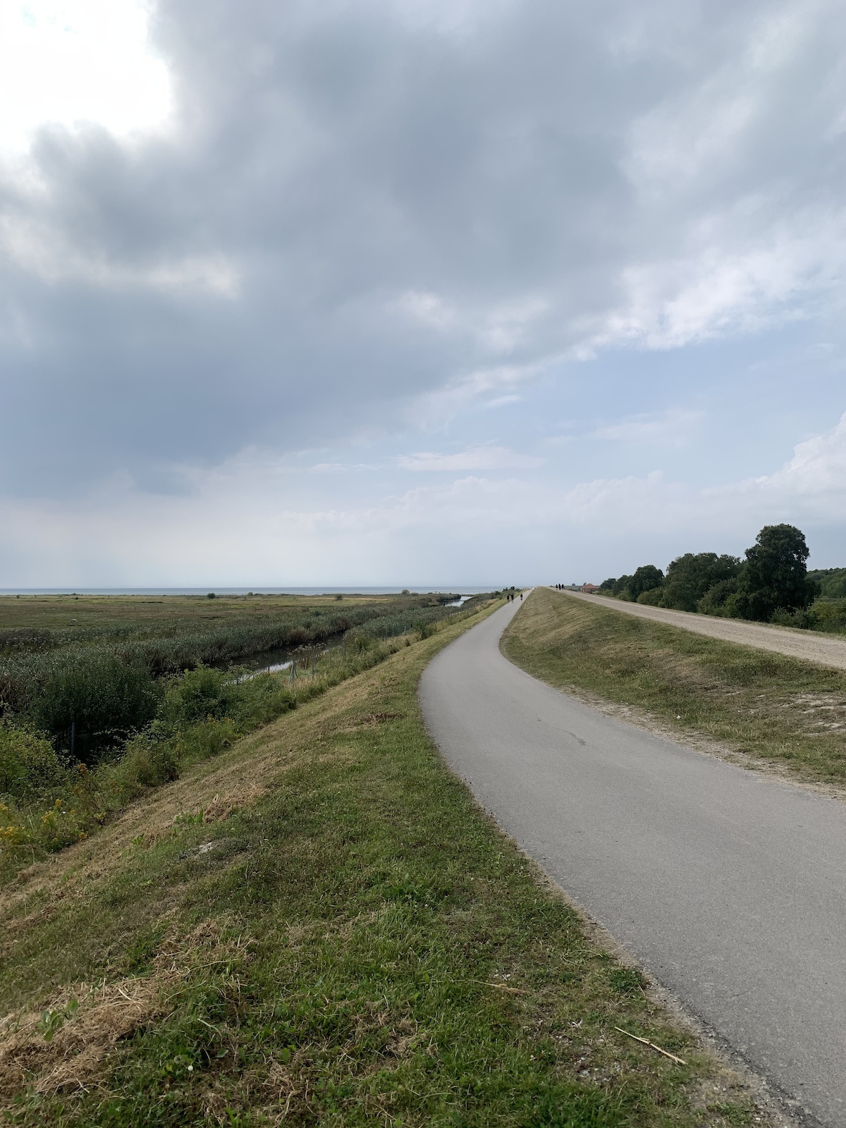 A flat paved path following a canal through open grassland.