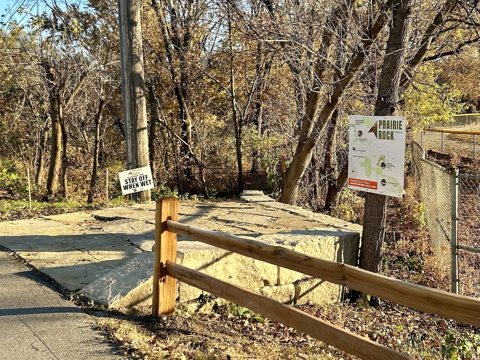 A trail sign and wooden fence at a forest trailhead entrance with fall foliage.
