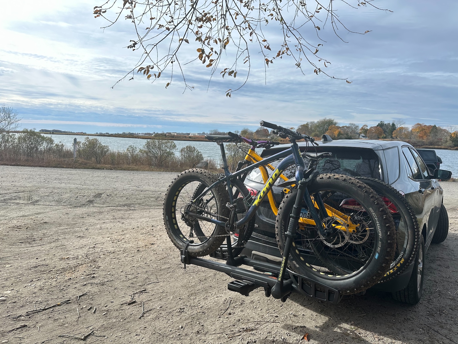A vehicle with fat bikes on a carrier at a parking area by a lake.