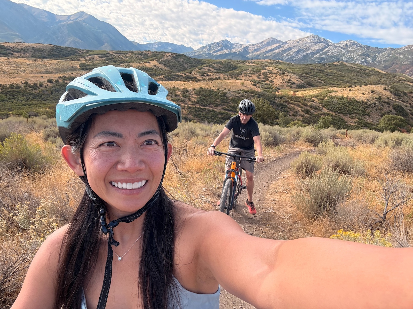 Two cyclists posing for a selfie in a desert landscape with mountains.