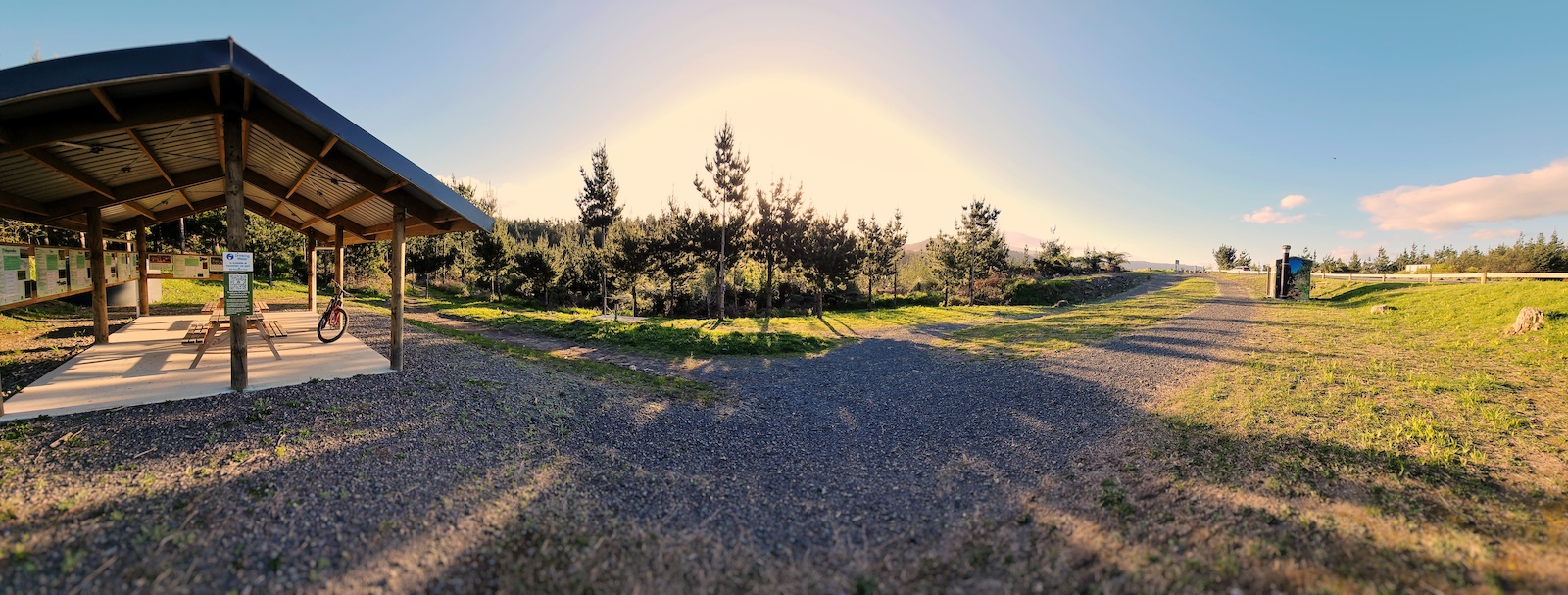 A parking area with a shelter, bike racks, and open grassy field at dusk.
