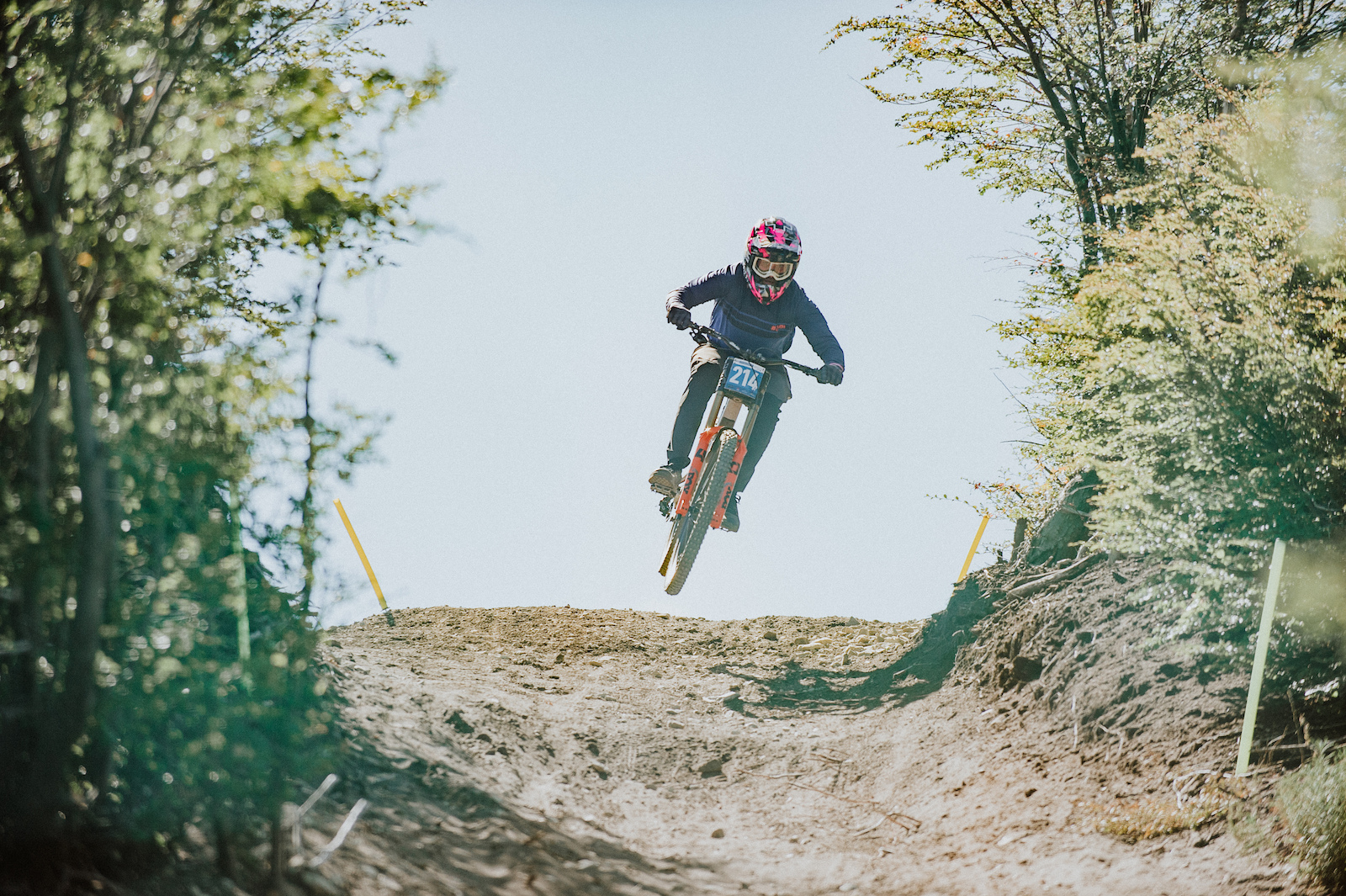A mountain biker in the air off a dirt jump in a forested area.