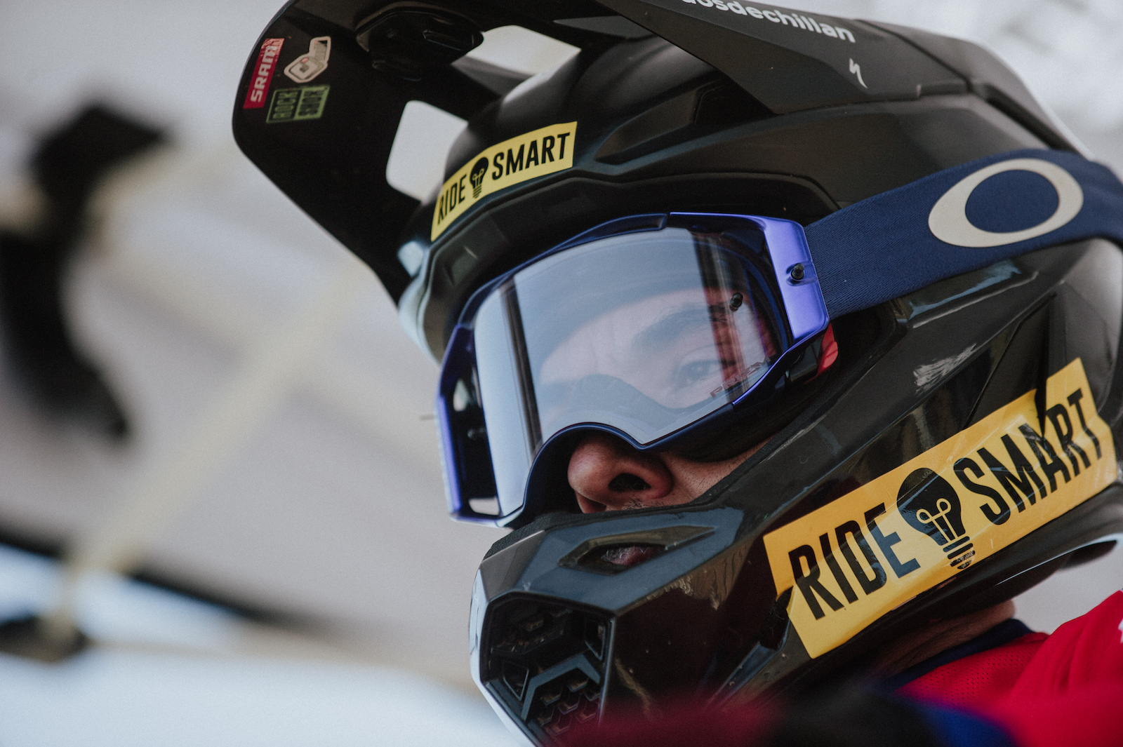 A close-up of a person wearing a black and yellow motocross helmet with goggles and red gear.