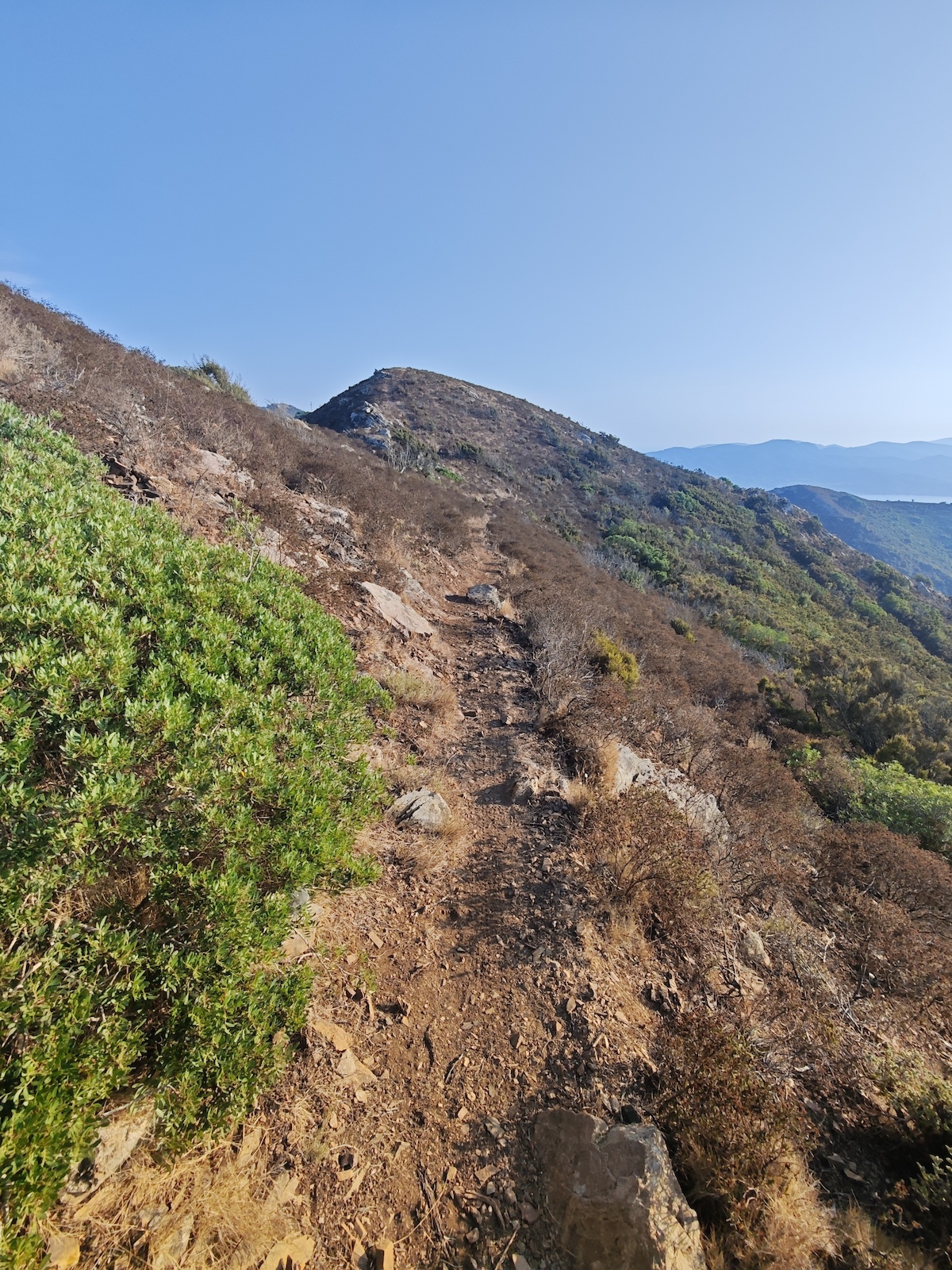 A hiker on a rocky ridge with mountains and valleys visible in the distance.